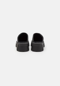 Chaussures noires à plateforme épaisse sans lacets vues de dos sur un fond blanc uni.