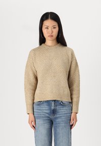 Maglione beige a maglia con un motivo testurizzato, colletto rotondo e polsini e orlo a coste. Abbinato a jeans blu chiaro a gamba dritta.