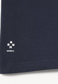 Mörkblå T-shirt i mjuk bomull, med en liten vit logotyp som s äger "DANIILM" nära nederkanten, med rena söms detaljer.