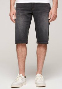Pantalones cortos de mezclilla oscura con un ajuste relajado, longitud a mitad del muslo, costuras en contraste y cinco bolsillos, combinados con zapatillas blancas.