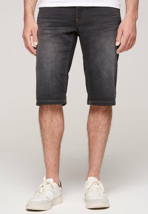 Shorts en denim foncé avec une coupe décontractée, longueur mi-cuisse, coutures contrastées et cinq poches, associés à des baskets blanches.