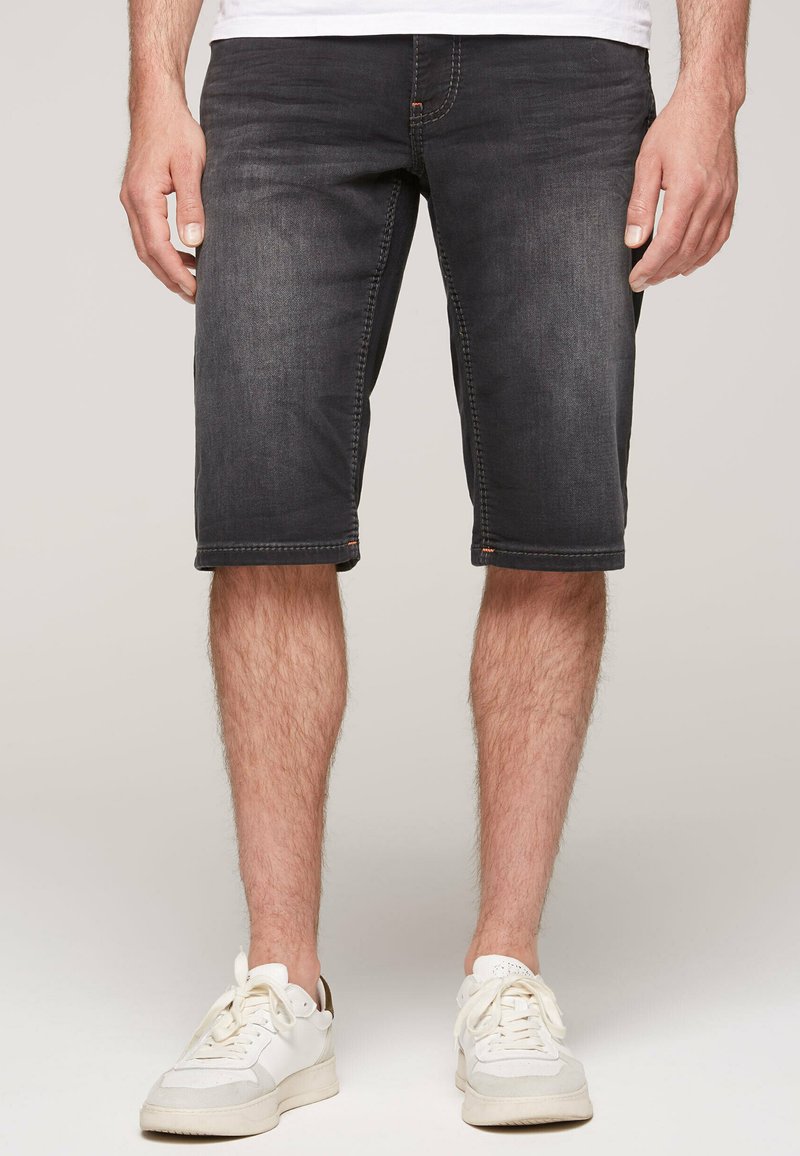 Donkerdenim shorts met een relaxte pasvorm, middenboven de dij, contrasterende stiksels en vijf zakken, gedragen met witte sneakers.