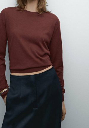 Pull en tricot bordeaux avec un col rond et des manches longues, associé à une jupe en satin bleu foncé présentant une texture lisse et un éclat subtil.