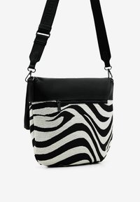 Mustavalkoinen seeprakuosiset laukku, jossa on nahkainen yläosa, säädettävä olkahihna ja vetoketjullinen etutasku. Karhea kangas ja tyylikäs muotoilu.