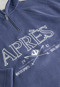 Navy fleece pullover with a quarter-zip collar. Front features white embroidered text “APRÈS”, “WINTER SPORTS”, and design accents.