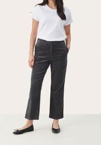 Pantalon en velours côtelé gris à jambes droites, avec poches devant et taille élastiquée. Associé à un t-shirt blanc uni et des chaussures plates noires.