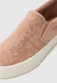 Sko med slip-on i myk rosa stoff med en snøre-lignende tekstur, med en hvit gummisåle. Designet har minimal søm og ingen snørebånd.