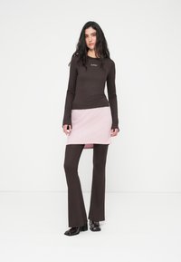 Καφέ μπλούζα με μακριά μανίκια και ριμπ υφή, συνδυασμένη με ροζ μίνι φούστα και καφέ καμπάνα παντελόνια. Επιβλητικές μαύρες γυαλιστερές μπότες με τακούνι.