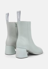 Botines azul claro hechos de cuero suave, con cremallera lateral y un tacón ancho y angular. Incluyen lengüetas de tela en forma de lazo para facilitar su uso.