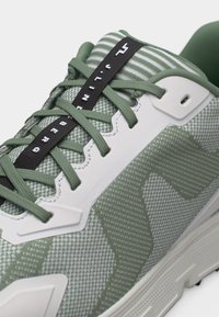 Detailný záber na zelenú a bielu športovú obuv s vzorovanou sieťovinou, zelenými šnúrkami a čiernym pruhom na jazyku s nápisom "JORDAN BERG".