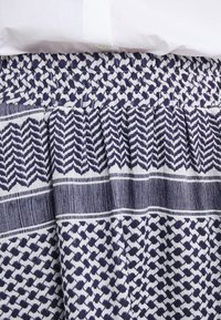 Tela con patrón en azul marino y blanco, con una cinturilla elástica texturizada. Presenta diseños en zigzag y puntos en un estilo plisado.