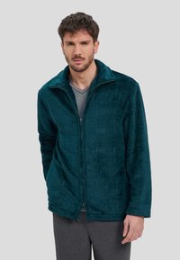 Chaqueta de forro polar azul verdoso con textura acolchada y cuello alto. Presenta cuadros sutiles, mangas largas y un ajuste holgado.