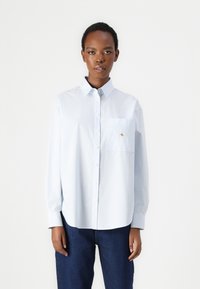 Striped blue and white long-sleeve shirt with a button-up collar, featuring a front pocket and embroidered logo detail on the pocket.