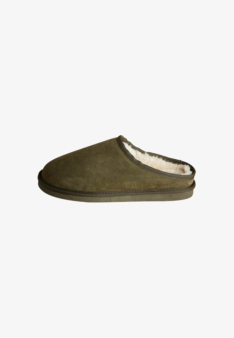 Pantofola in suede verde oliva con morbida fodera beige e punta arrotondata. Presenta una suola piatta e testurizzata e delicate cuciture lungo il bordo.
