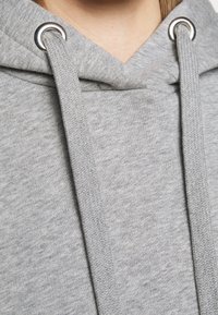 Close-up van grijze hoodie stof met dikke koorden die door metalen oogjes bij de hals zijn geregen.