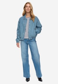 Světle modrá džínová bunda s volným střihem, elastickými manžetami a límečkem, doplněná pruhovaným tričkem a širokými džínami.