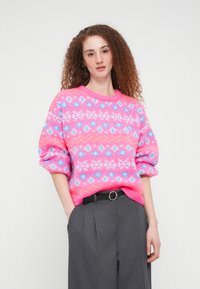 Πλεκτό πουλόβερ με φωτεινή ροζ βάση και γεωμετρικά σχέδια σε μπλε και λευκό. Σχεδιασμένο με άνετη εφαρμογή και ρεβέρ στα μανίκια.