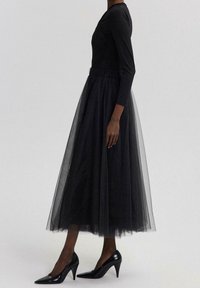 Zwarte lange mouwen top, gecombineerd met een doorzichtige zwarte tule rok. De outfit heeft een aansluitend lijfje, een elastische tailleband en zwarte puntige hakken.