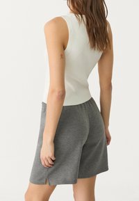 White ribbed tank top paired with gray knit shorts. The shorts have side slits and an elastic waistband. Soft texture, casual fit.
