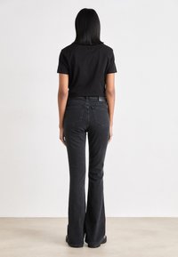 Camiseta preta cropped combinada com jeans pretos de cintura alta e flare, apresentando bolsos traseiros e um tecido texturizado para uso casual.