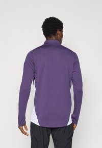 Purple long-sleeve polo shirt with a white side panel. Features a stand-up collar and a smooth, stretchy fabric texture.