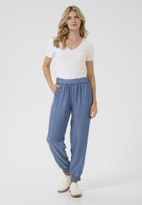 Joggers de mezclilla azul ligeros con cinturilla elástica y puños acanalados, combinados con una blusa blanca de mangas cortas con un diseño arrugado.