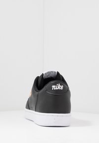 Svart sneakers med övre del i texturerat läder, vit sula och svart mesh-fodring. Har en vit "Nike"-logotyp på hälen och sidan.