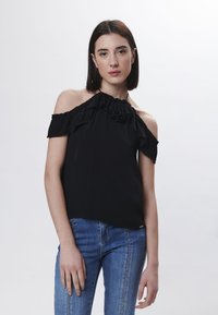 Top nero con spalle scoperte, design arricciato e dettagli floreali sul colletto, abbinato a jeans in denim blu dal fit aderente.