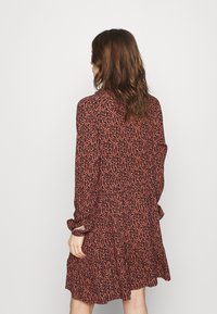 Šaty s dlouhým rukávem v černé barvě a korálovém květinovém potisku. Vyrobeny z lehkého materiálu se zvonovým lemem a zapínáním na knoflíky, s volným střihem.