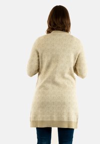 Suéter de punto beige con un patrón texturizado, que presenta un cuello redondo y mangas largas, que llega más allá de las caderas, combinado con vaqueros azules.