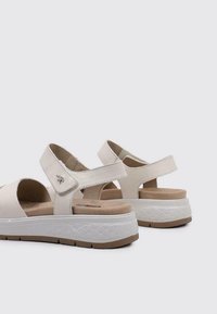Sandalias beige con parte superior de cuero suave, diseño abierto, correas ajustables, plantilla acolchada y suela de plataforma blanca texturizada.