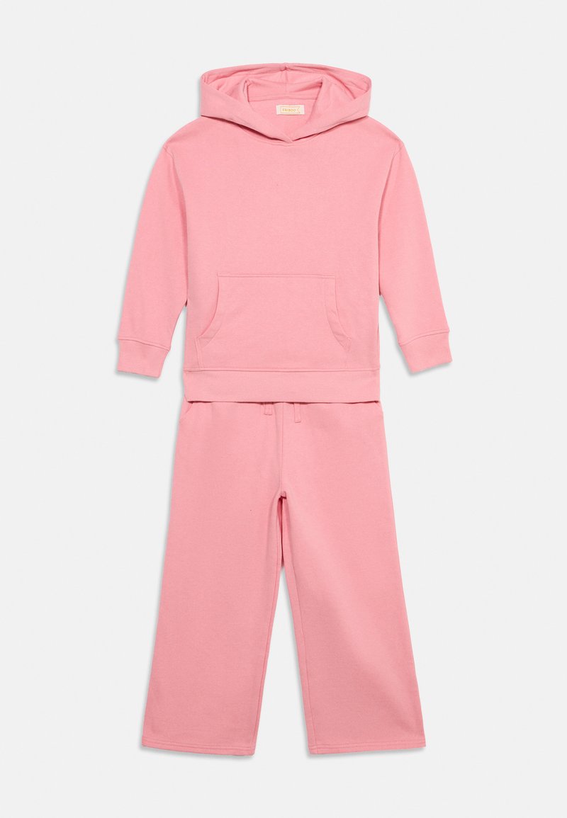 Sweat-shirt rose à capuche avec poche avant et pantalon ample assorti sur un fond uni.