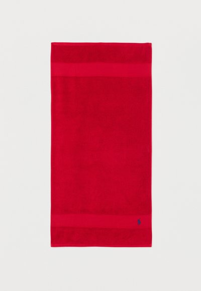 Rødt rektangulært håndklæde med to vandrette bånd nær kanterne og et lille blåt broderet logo i nederste højre hjørne.