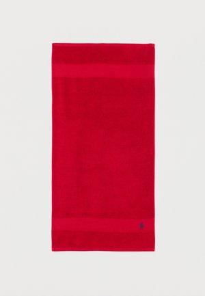 Serviette rectangulaire rouge avec deux bandes horizontales près des bords et un petit logo brodé bleu dans le coin inférieur droit.