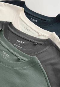 Drie gevouwen t-shirts in verschillende kleuren: donkergroen, grijs en crème, met de labels "NEXT" en "M REGULAR FIT" op de neklijnen.