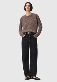 Brun strikket sweater med et tekstureret mønster, kombineret med højtaljede sorte jeans og sorte flade sko med en gulddetalje.