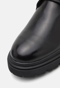 Gros plan sur le bout d'une botte en cuir noir avec une semelle épaisse en caoutchouc texturé et une finition lisse et polie.