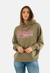 Olijfgroene hoodie met roze grafische tekst en logo. Bevat een ruime capuchon, geribbelde manchetten en een patch op de linkermouw. Gemaakt van katoen.