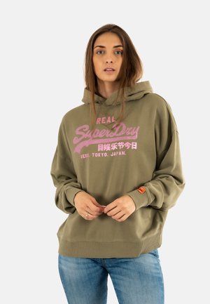Sudadera verde oliva con texto gráfico y logotipo en color rosa. Presenta una capucha amplia, puños acanalados y un parche en la manga izquierda. Material de algodón.