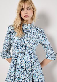 Langärmliges Kleid mit blau-weißem Blumenmuster, Kragen und gebundenem Taillendetail. Hergestellt aus leichtem Stoff.