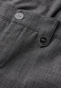 Tissu gris avec un motif à carreaux subtil, comportant deux boutons noirs et une texture lisse. Les boutons sont centrés sur la section de la taille.