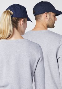 Graue Sweatshirts mit Rundhalsausschnitten, kombiniert mit marineblauen Baseballkappen, getragen von zwei Personen von hinten.