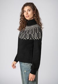 Schwarzer Strickpullover mit hohem, geripptem Kragen. Verfügt über ein geometrisches Creme-Muster an der Schulterpartie. Weicher Stoff und lockere Passform.