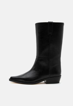 Sort læder cowboystøvle til midt på læggen med spids tå, lav stablet hæl og trækkestrop øverst mod en ensfarvet baggrund.