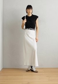 Black short-sleeve top, white long skirt, silver belt, shiny silver ankle boots. Neutral background with wooden floor, minimalist design.