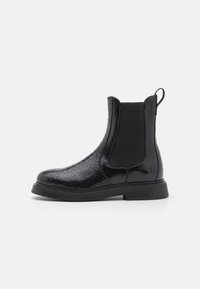 Svart Chelseaboot i texturerat läder med en slät panel, elastiska insatser och en dragflik; platt gummisula.