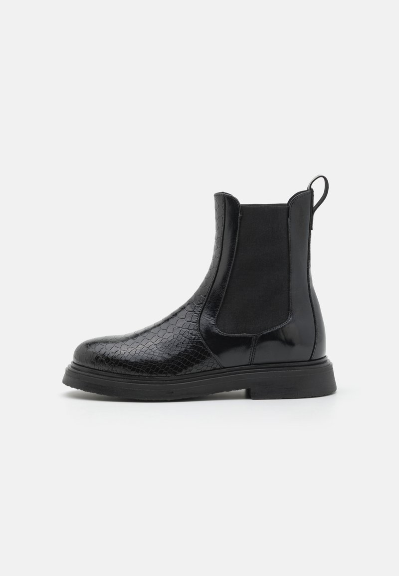 Svart Chelseaboot i texturerat läder med en slät panel, elastiska insatser och en dragflik; platt gummisula.