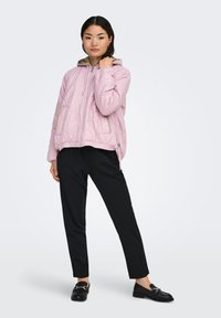 Vaaleanpunainen tikattu takki, jossa on huppu, beigenvärisillä yksityiskohdilla ja etuvetoketjulla. Yhdistetty mustiin housuihin ja mustiin loafereihin.