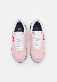 Baskets rose clair avec tige perforée, lacets blancs, accents violets et semelle bleu marine. Présente le logo GAP sur la languette et le côté.