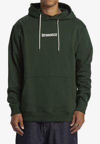 Felpa verde scuro realizzata in tessuto morbido, con tasca frontale, cordini color crema e testo del logo bianco sul petto.